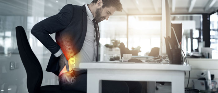 man sitting at desk holding his lower back in pain